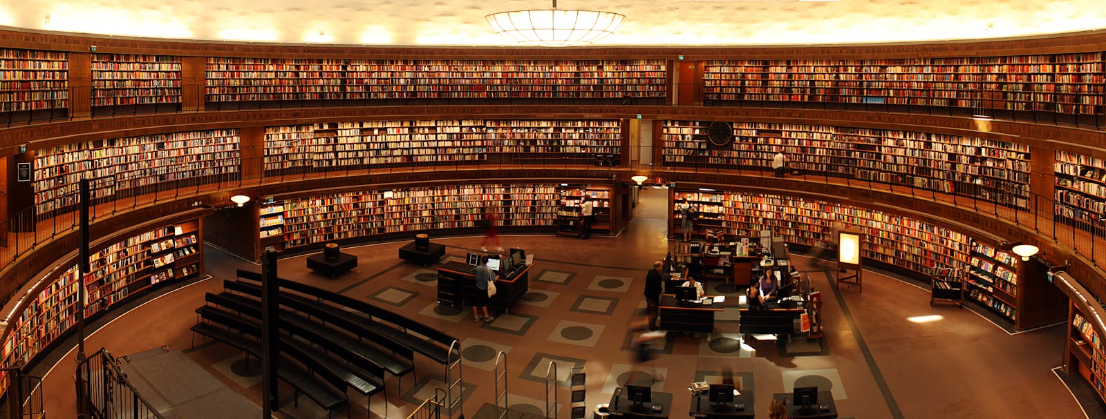 Panoramic view of a grand circular library with shelves full of books and study desks.