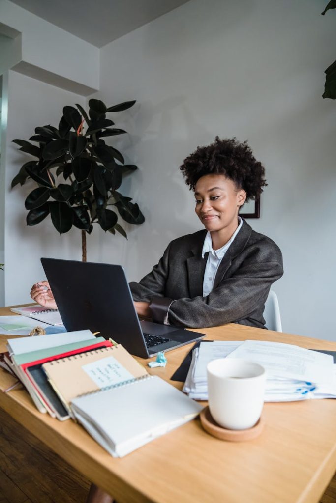 Smiling woman working on a laptop with office documents around, creating a productive workspace vibe.