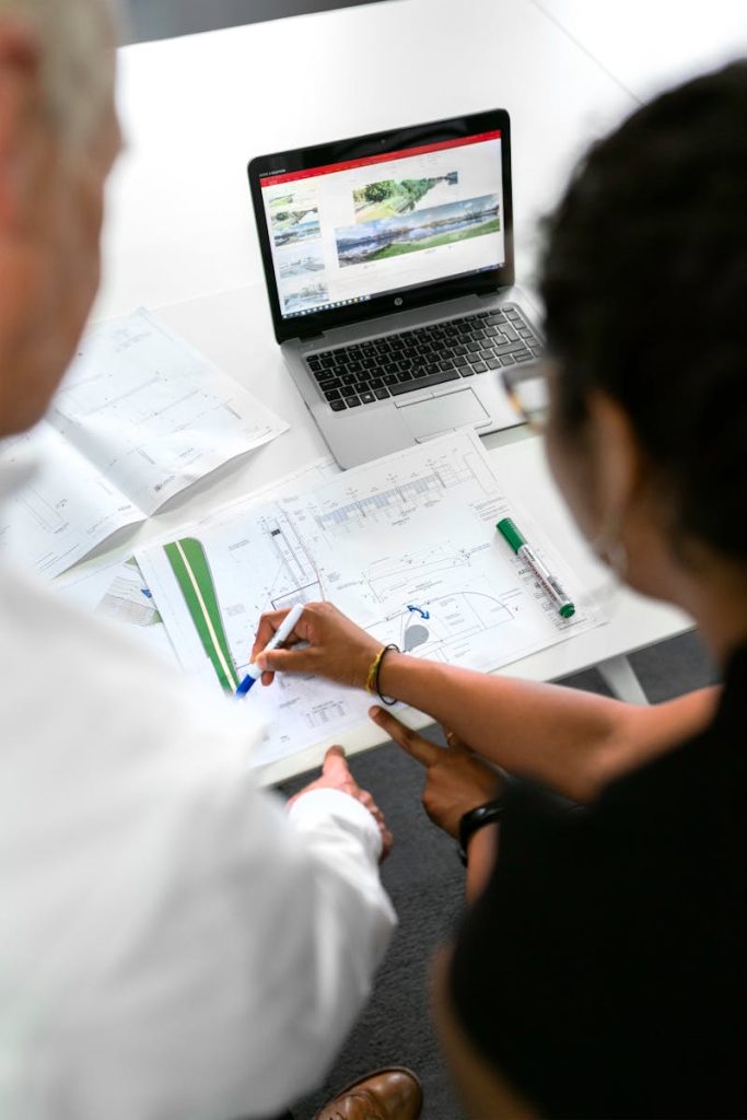 Engineers collaborate on designs with blueprints and laptops in a modern office setting.