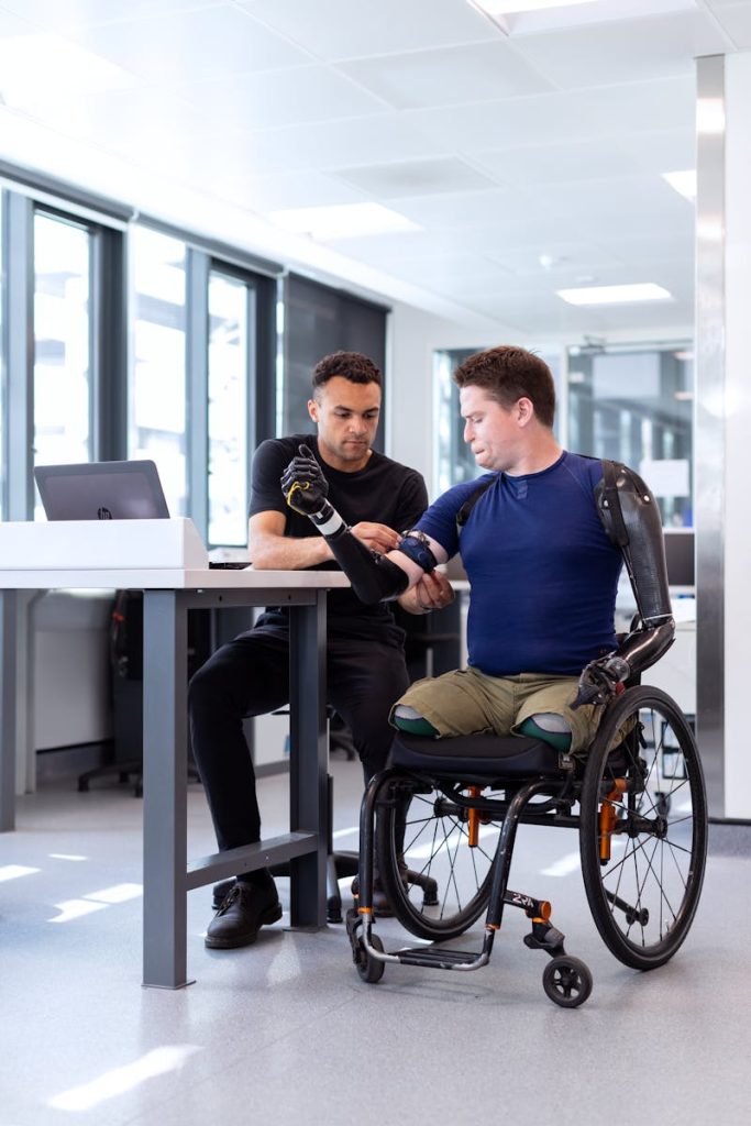 Engineer adjusts prosthetic arm for seated man in wheelchair, focusing on modern technology in healthcare.