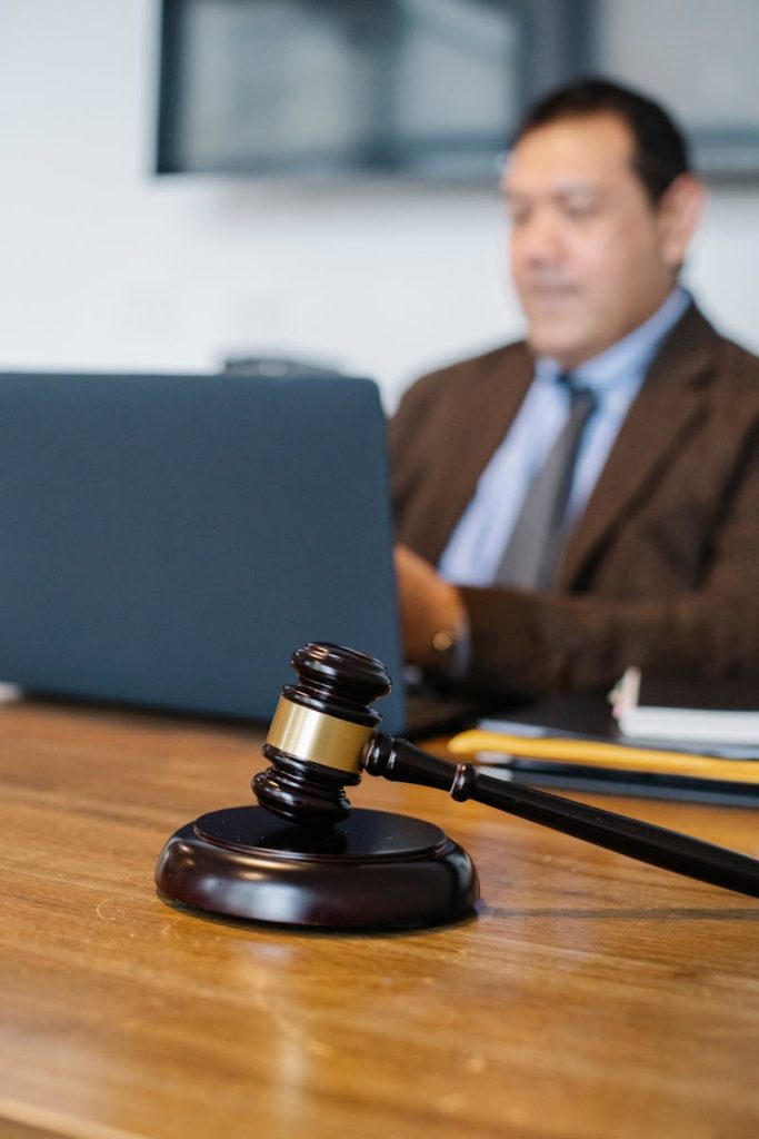 A focused lawyer working on a laptop with a gavel on the desk, indicating legal proceedings.