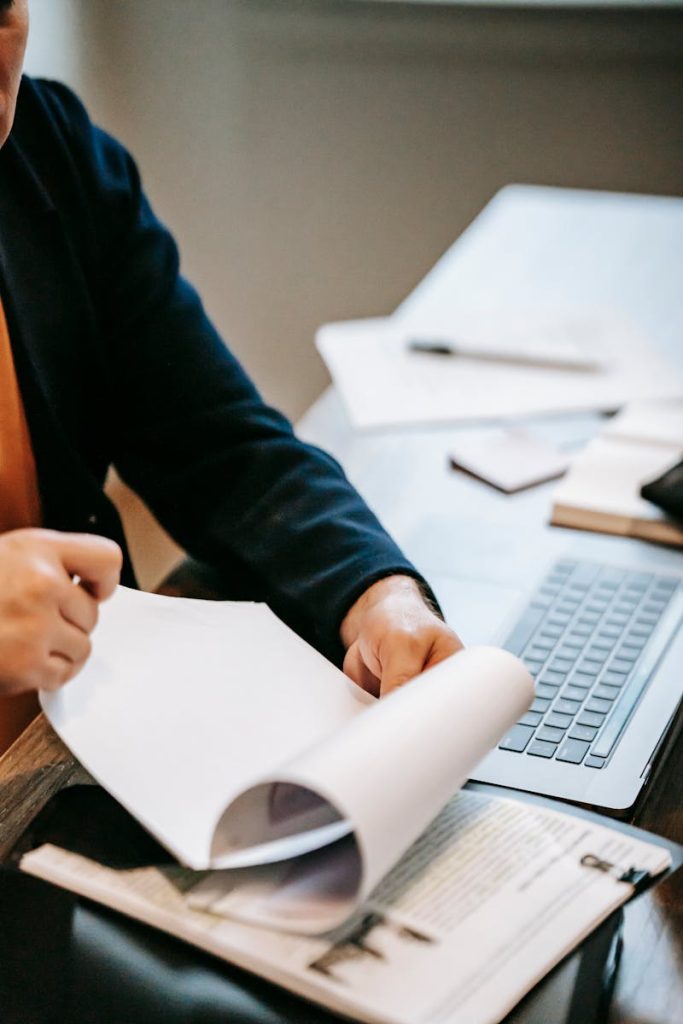 Person reviewing documents with laptop for work analysis.
